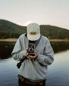 a person standing in front of a body of water holding a camera