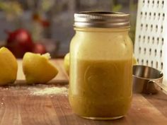 a jar filled with yellow liquid sitting on top of a wooden table next to two lemons