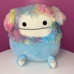 a stuffed animal with multicolored fur on it's head and legs sitting on a table