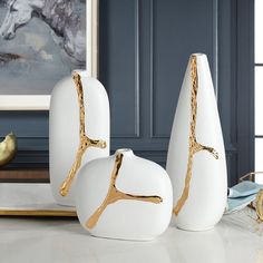 three white and gold vases sitting on top of a table next to a painting