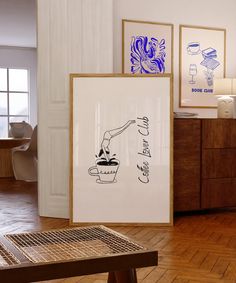 two framed art pieces on the floor in a room with wooden floors and white walls