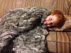 a little boy laying on top of a couch covered in a furry gray fur blanket