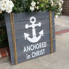 a wooden sign that says anchored in christ with an anchor on it and white flowers