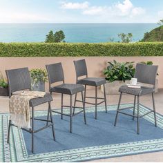 four chairs and a rug on a patio with the ocean in the backround