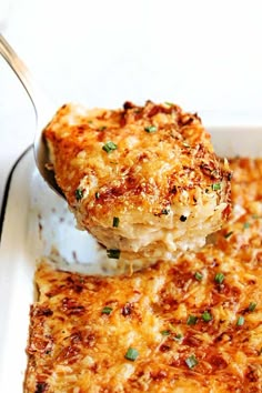 a close up of a casserole dish with a spoon full of cheese and green onions