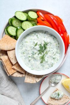 a bowl of dip surrounded by crackers and vegetables