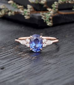 a tan gold ring with a blue sapphire and diamond shoulders on a wooden table next to flowers