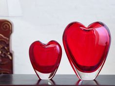 two red heart shaped vases sitting on top of a table next to a lamp