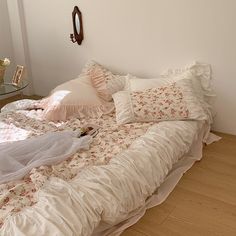 an unmade bed with white sheets and pink flowers on the bedspread next to a glass table