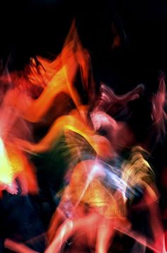 blurry photograph of people dancing in the dark with colored lights on them and black background