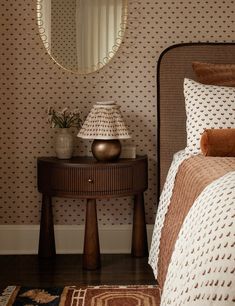 a bed room with a neatly made bed and a round mirror on the wall above it