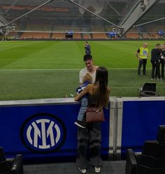 a woman holding a baby standing next to a man on a soccer field at night