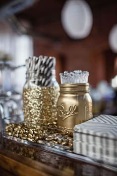 gold and silver items are sitting on a table with striped napkins, glass jars and paper straws