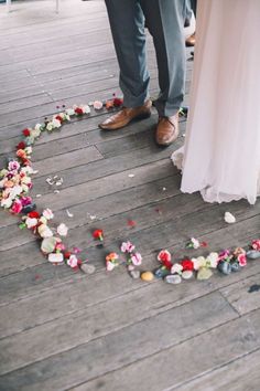 a couple standing next to each other in front of a heart made out of flowers