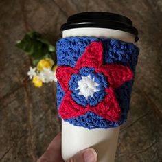 a hand holding a coffee cup with a crocheted flower on it