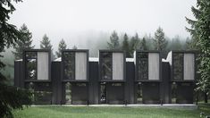 a row of black buildings sitting on top of a lush green field next to trees