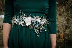 a woman wearing a green dress with white flowers on it's belt and holding her hands in her pockets