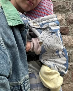 a woman holding a baby in her arms and wearing a blue jean jacket over it