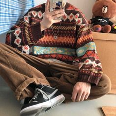 a man sitting on the floor taking a selfie with his cell phone and wearing a sweater