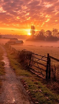 the sun is setting over a field with a fence and barn in the distance,