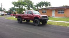 a red pick up truck parked on the side of a road in front of a house