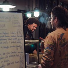 two men standing next to each other in front of a whiteboard with writing on it