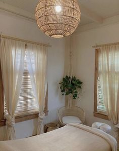 a bedroom with a bed, wicker chair and hanging lamp in the corner next to two windows