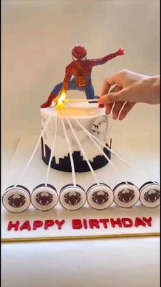 a spiderman birthday cake is being held by someone's hand over the top of it