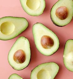 an avocado cut in half on a pink surface