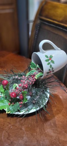 a white vase filled with berries and greenery on top of a wooden dining room table