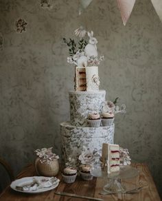 a three tiered cake sitting on top of a table next to cupcakes