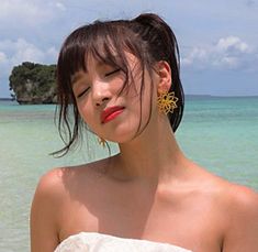 a woman standing in the ocean with her eyes closed and wearing large gold earrings