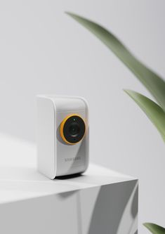 the camera is sitting on top of a white shelf next to a green potted plant