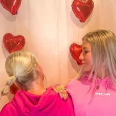 two women standing next to each other in front of heart shaped balloons