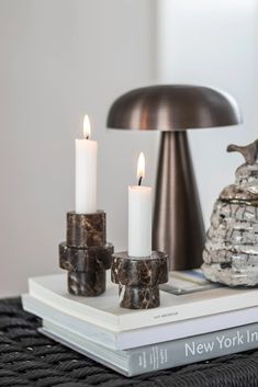 two candles are sitting on top of a stack of books next to a table lamp