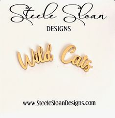 two wooden name earrings with the words wild cats on them in gold color, set against a white background