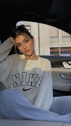 a woman sitting in the passenger seat of a car wearing a nike sweatshirt and jeans