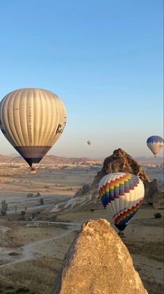 several hot air balloons flying in the sky above some rocks and dirt fields with mountains in the background