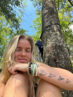 a woman with tattoos on her arm sitting next to a tree and looking at the camera