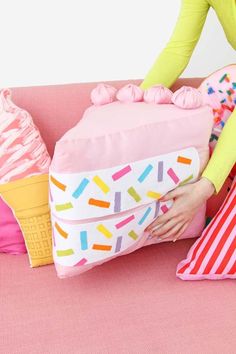 a woman sitting on a pink couch holding an ice cream cone pillow