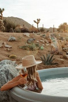 a woman sitting in a hot tub holding a glass of wine and looking at the desert