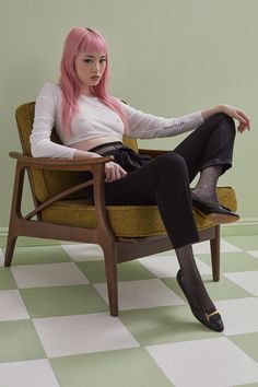 a woman with pink hair sitting on a chair in a green and white checkered floor