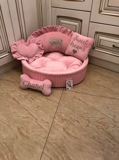 a pink dog bed in the corner of a kitchen with a bone toy on the floor