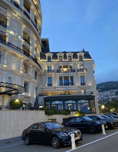 several cars parked in front of a hotel at night with lights on the windows and balconies