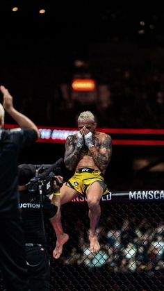 a man standing on top of a cage next to another man holding a boxing glove