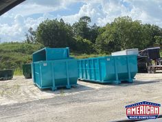 two blue dumpsters sitting on top of a dirt field