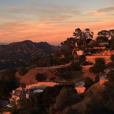 the sun is setting over some hills and houses