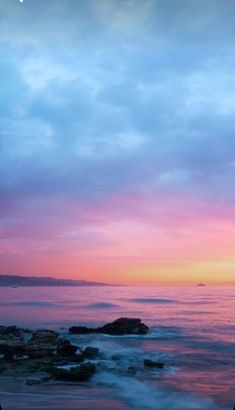 the sun is setting over the ocean and rocks