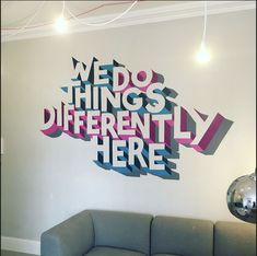 a couch sitting in front of a wall that has words on it and the word we do things differently here