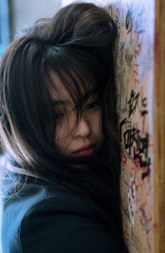 a woman leaning against a wall with graffiti on it's walls and looking down